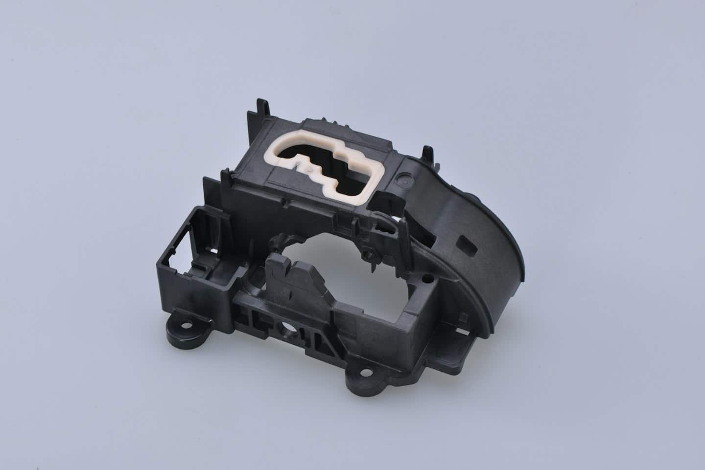 Black and white molded plastic automotive gear shifter component.